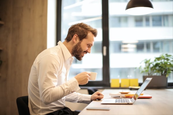 Man on laptop drinking coffee and smiling